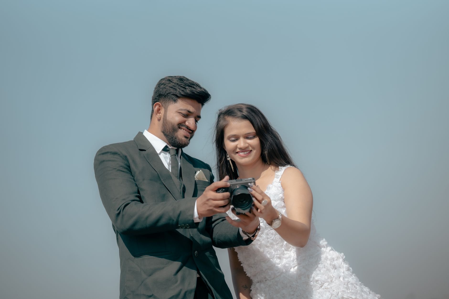 Smiling couple reviewing photos on a camera during an outdoor pre-wedding shoot.