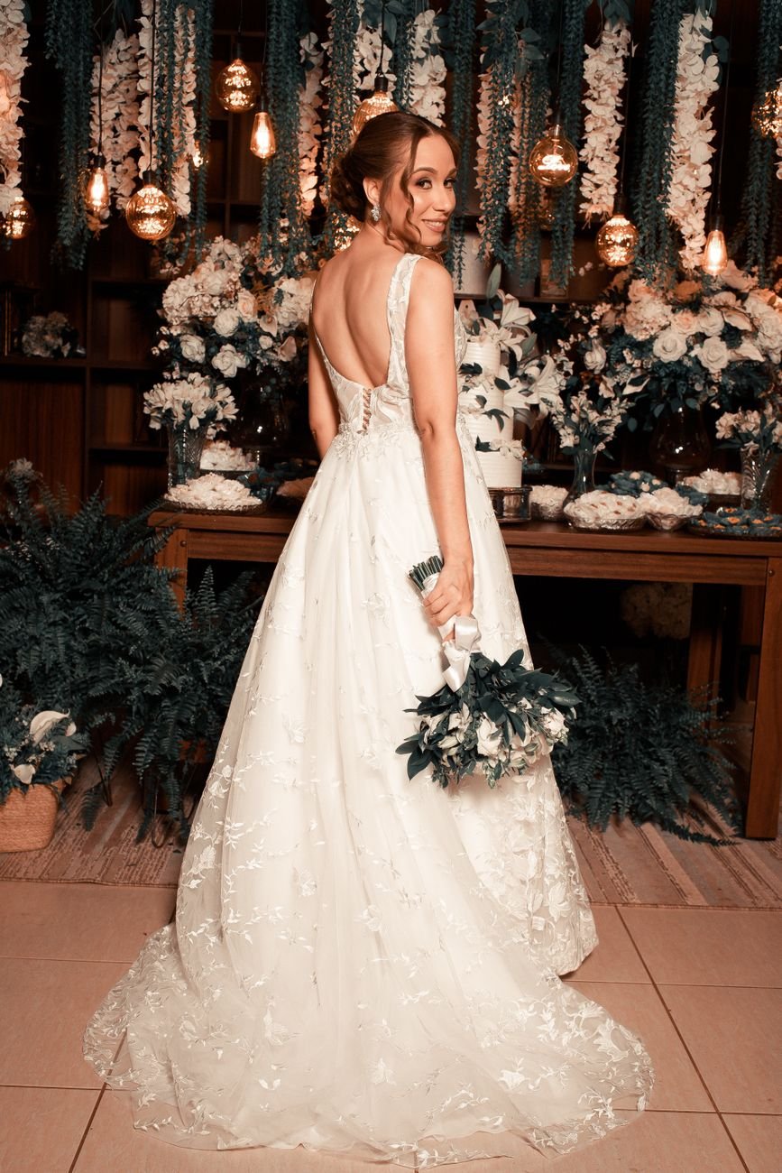 Bride in a lace gown holding a bouquet at a decorated indoor wedding venue.